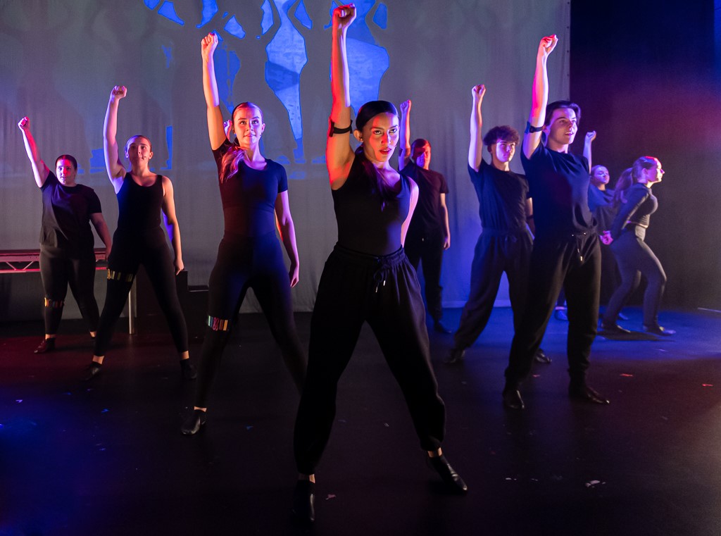 Rosa performing stood with one arm in the air with a group of students.