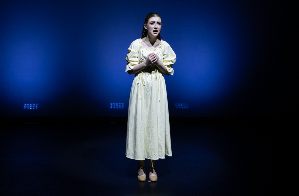 One dancer wearing a log white dress with their hands clasped together in front of their chest