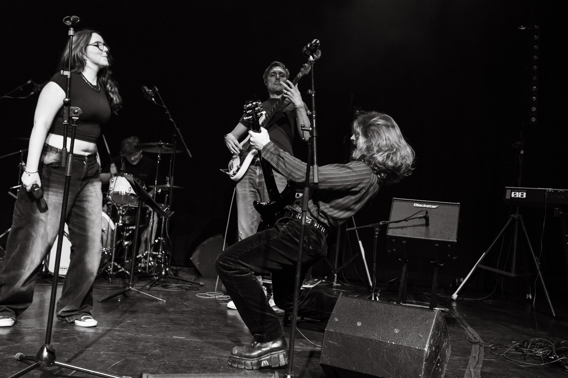 Students performing in their band on stage. The electric guitar player is bent back playing their guitar in the air.