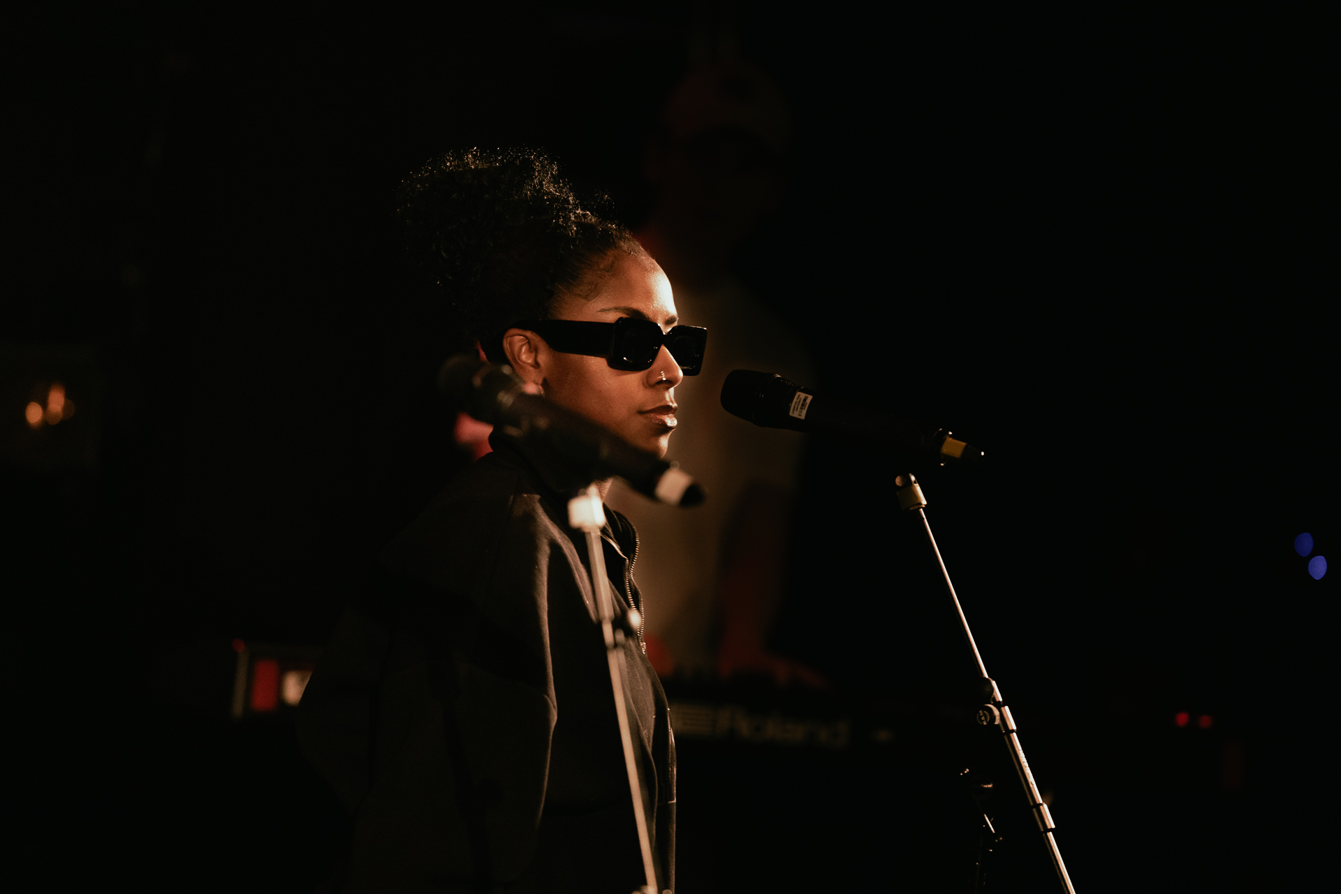 A student vocalist standing in front of a microphone with sunglasses on.