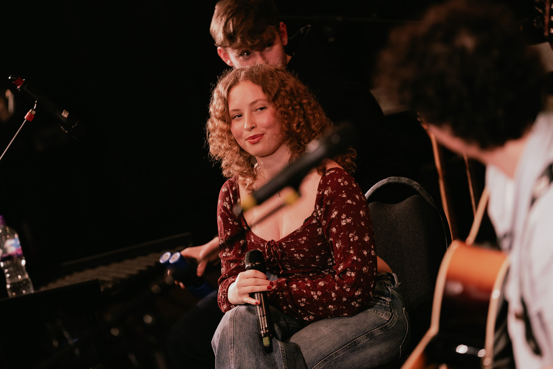 A student vocalist smiling at another student next to where who is playing an instrument.