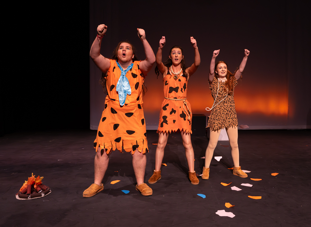 Three students with their arms in the air all, dressed in Flintstones cotumes