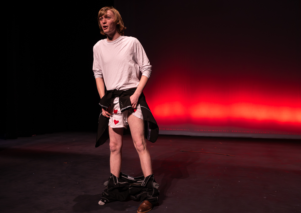 Student on stage with his pants around his ankles showing patterned underpants with hearts on them.